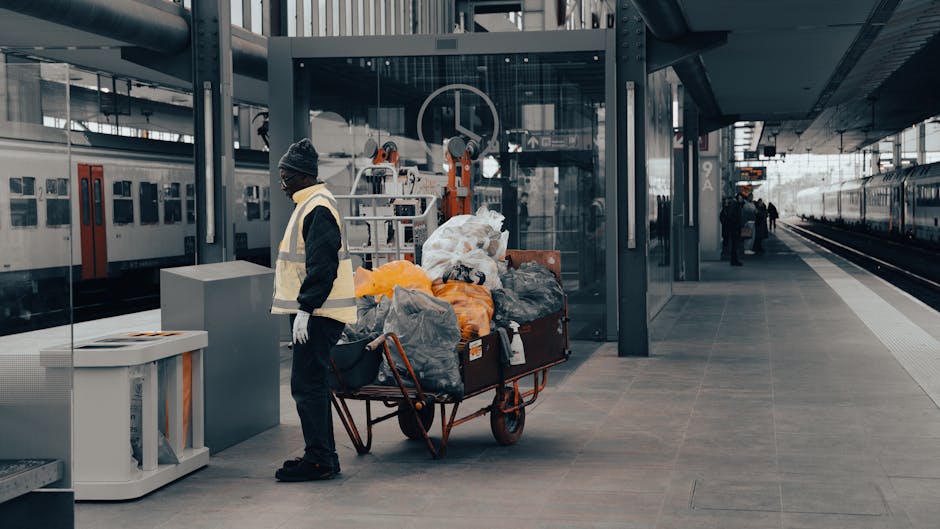 A person wearing orange cleaning gloves places or adjusts a lightbox sign on a table, with the illuminated message 'CLEANING HOME' displayed prominently. The background shows a blurred modern interior